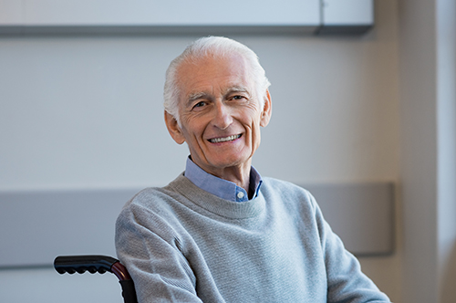 Senior man wearing grey sweater sitting in wheelchair smiling